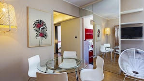 Uma sala de jantar moderna com mesa de vidro e cadeiras brancas, televisão na parede e obras de arte nas paredes.