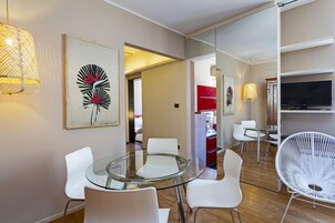 Un comedor moderno con mesa de vidrio y sillas blancas, televisión en la pared y obras de arte decorando las paredes.