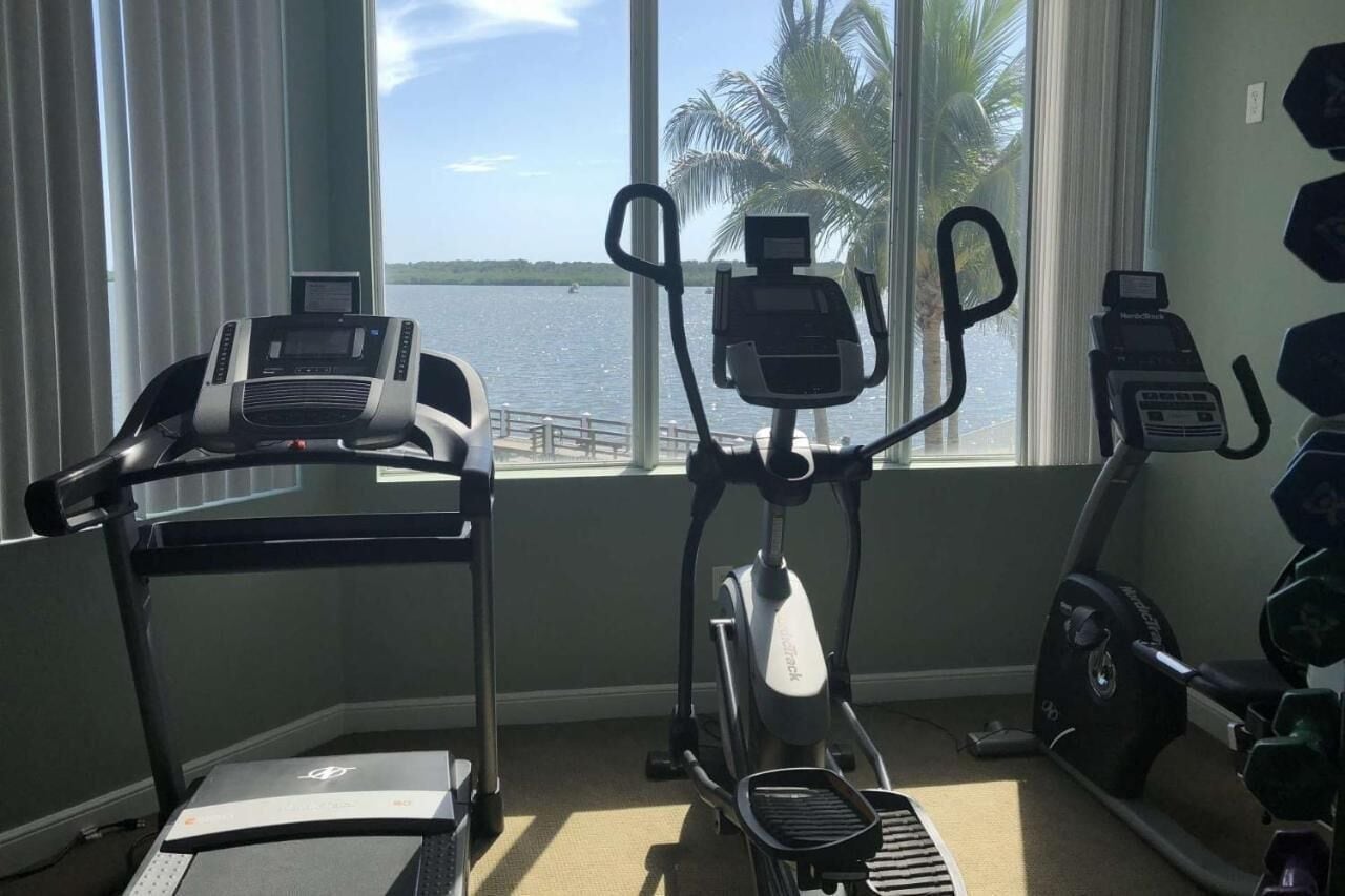 A home gym with exercise equipment, large windows, and a view of the water.