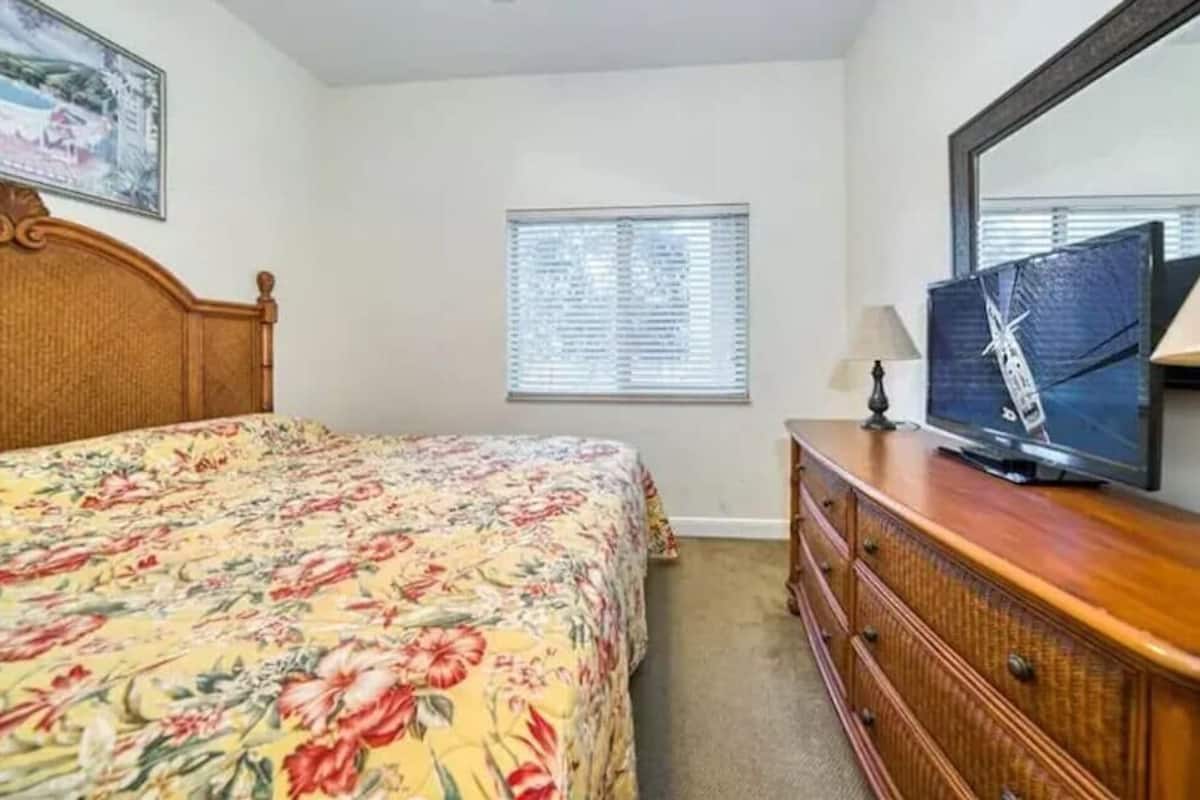 Un dormitorio con cama, cómoda, televisor y ventana.