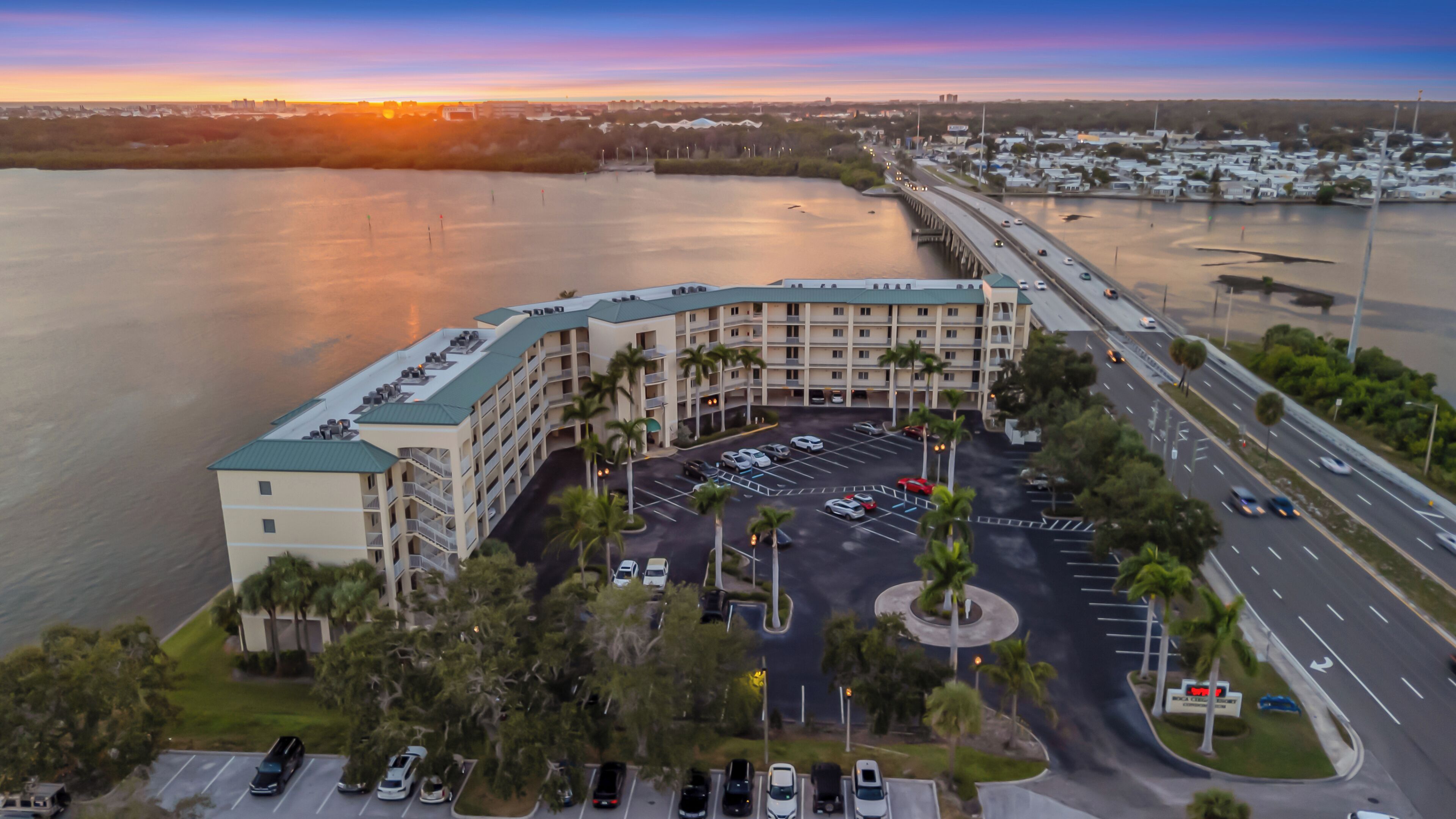 An aerial view of a hotel with a parking lot, a bridge, and a body of water.