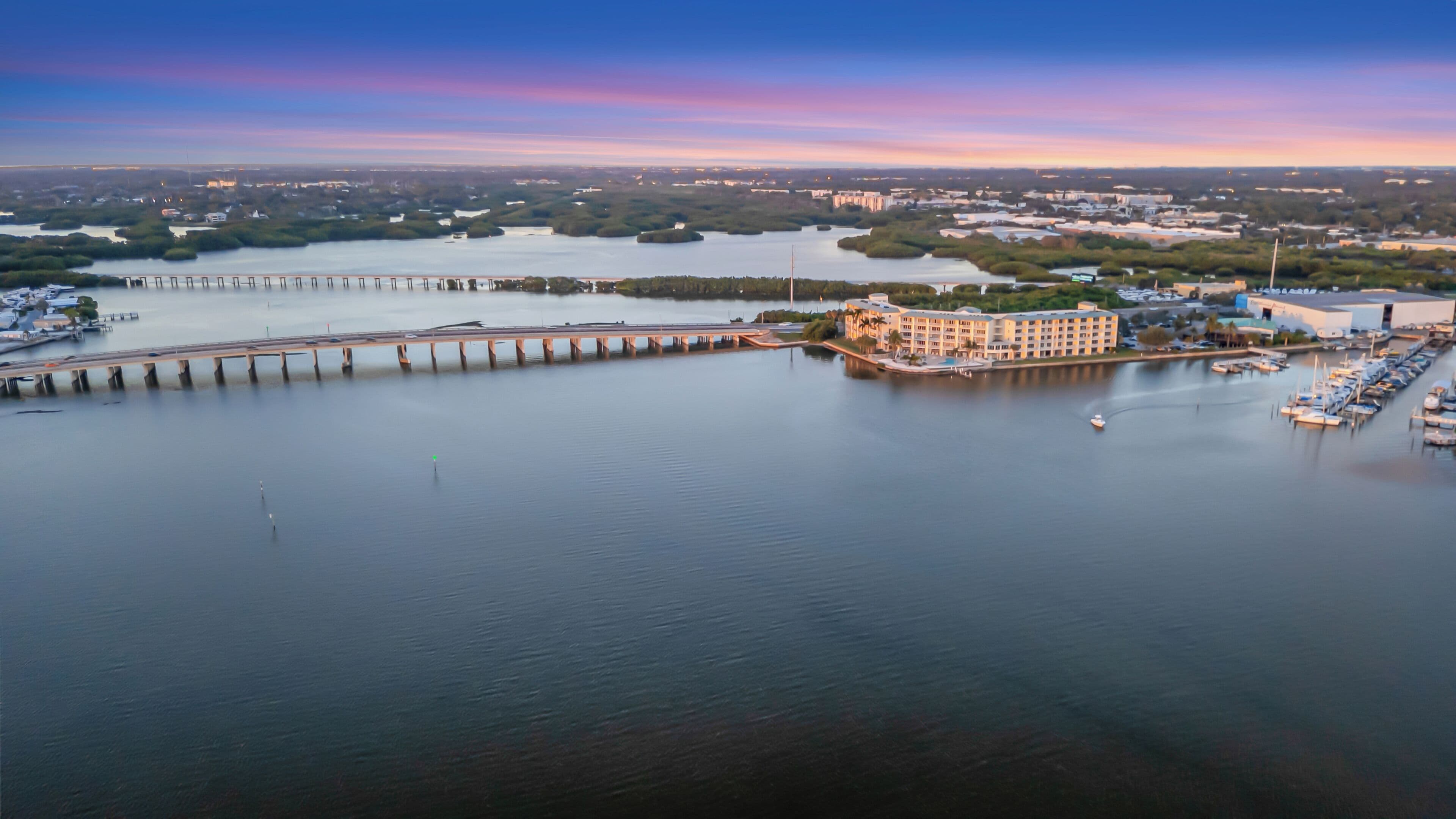 Vue aérienne d’une propriété située au bord de l’eau, comprenant un port de plaisance, une jetée et un bâtiment doté de nombreux balcons donnant sur l’eau.