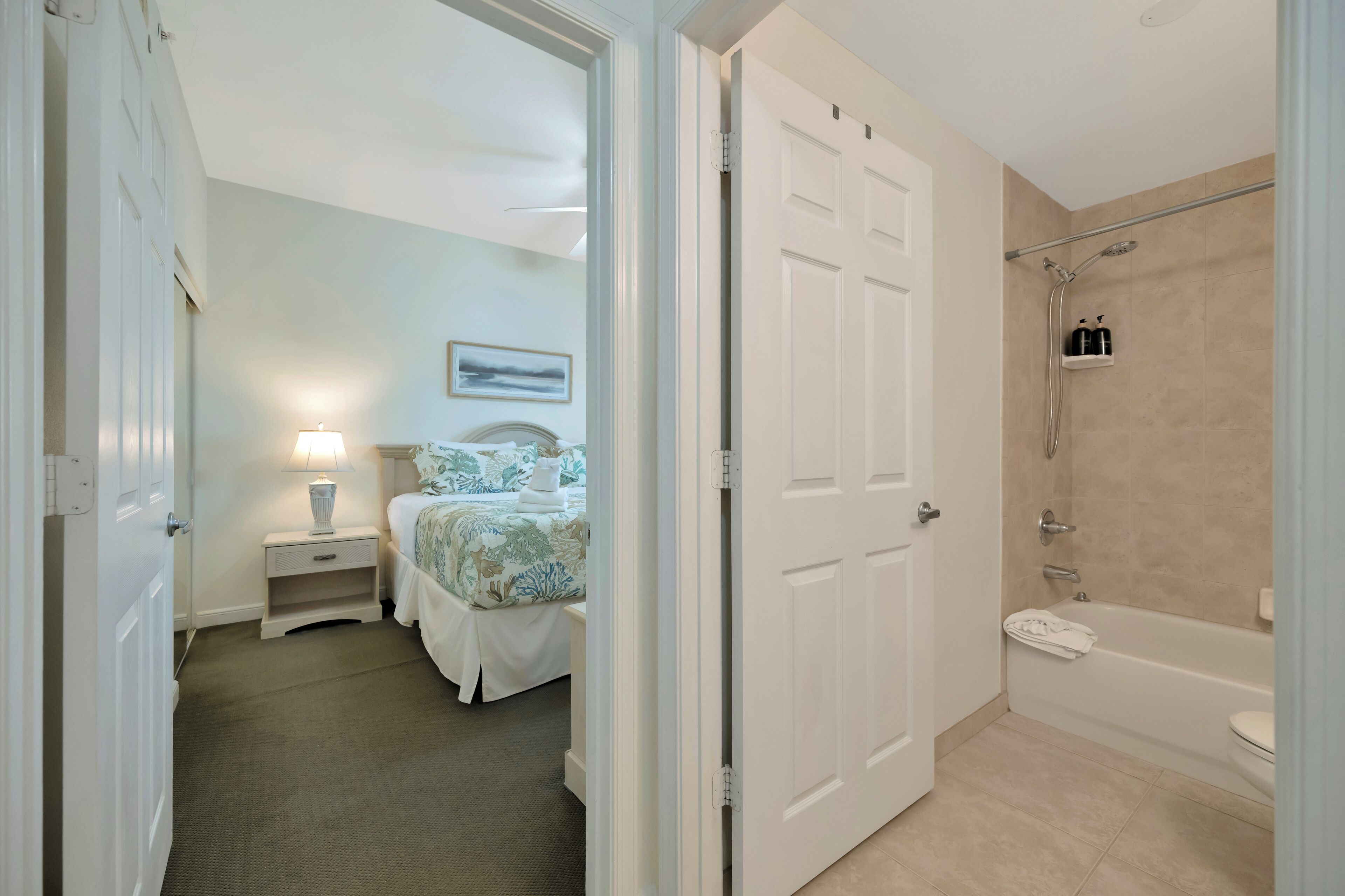 A hotel room with a bed, bedside table, lamp, and a bathroom with a shower and bathtub.