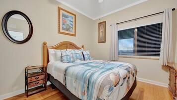 A bedroom with a bed, a nightstand, a mirror, and a window with blinds.