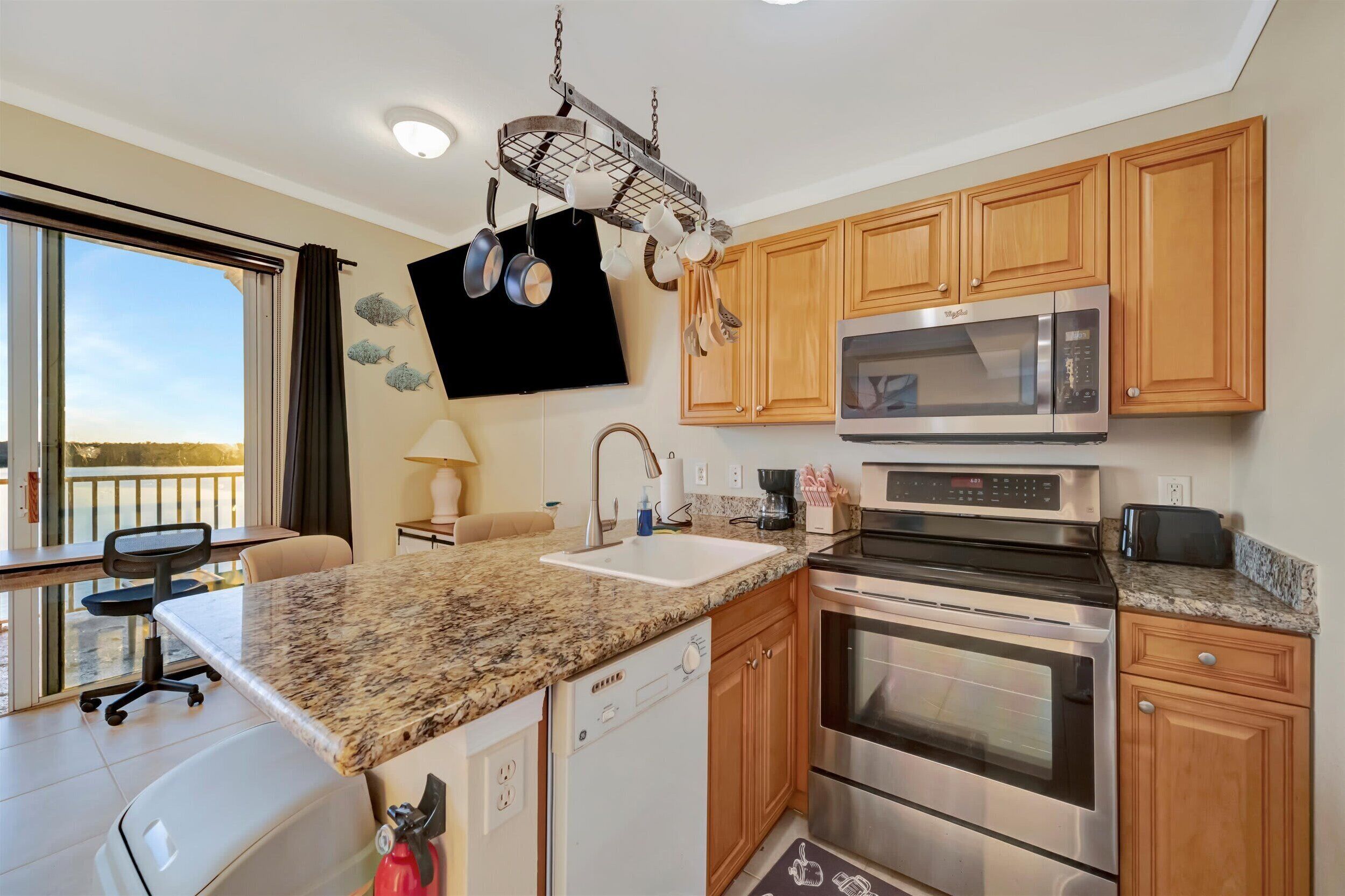 A modern kitchen with granite countertops, stainless steel appliances, wooden cabinets, and a hanging pot rack.