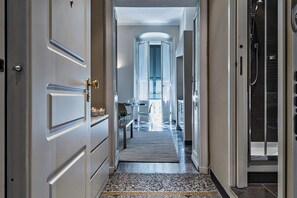 A hallway with a door on the left, a shower area on the right, and a dining area in the center with a table and chairs. - Via Roma Luxury Apartment by Wonderful Italy (Genoa)