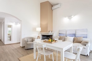 A modern living room with a white fireplace, a dining table with chairs, and a sofa. - Villino a Fontane Bianche by Wonderful Italy (Syracuse)