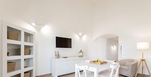 A modern, white-themed living space with a dining area, a sofa, and a TV mounted on the wall. - Villino a Fontane Bianche by Wonderful Italy (Syracuse)