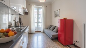 Una cucina compatta dal design moderno, con cappa in acciaio inox, frigorifero rosso e una ciotola di frutta sul piano di lavoro.
