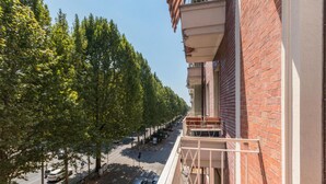 Una vista di strada con filari di alberi, un'auto rossa e un edificio con un balcone.
