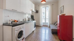 Una cucina compatta con lavatrice, un frigorifero rosso e un angolo ristoro con divano.
