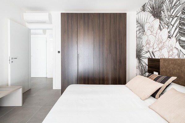 A bedroom with a large bed, a wooden wardrobe, and a wall with a tropical leaf pattern.