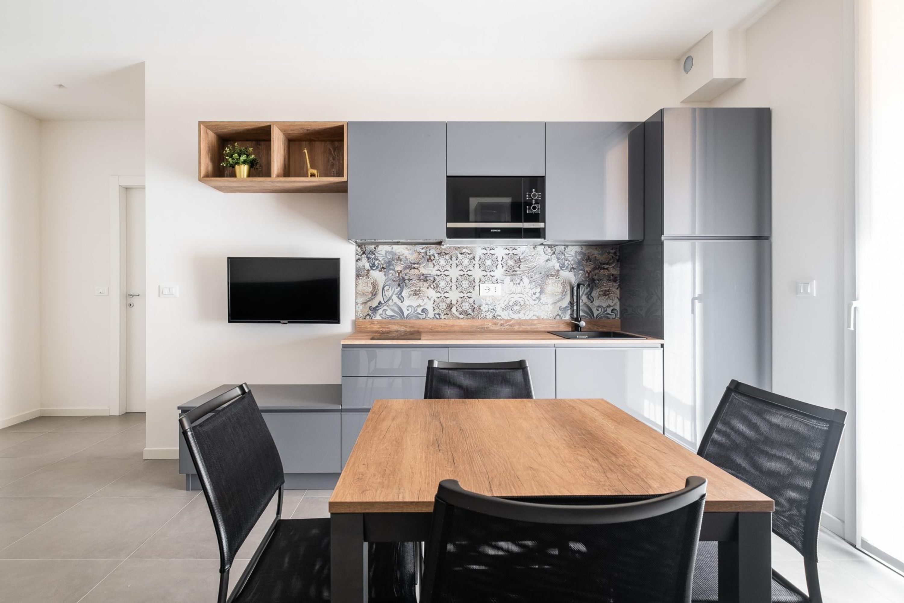 A modern kitchen with grey cabinets, a wooden dining table, and black chairs.