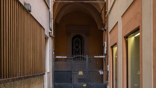 A narrow alleyway with a brick floor, a metal gate, and a building with a tiled archway. - Ariosti Apartment I by Wonderful Italy (Bologna)