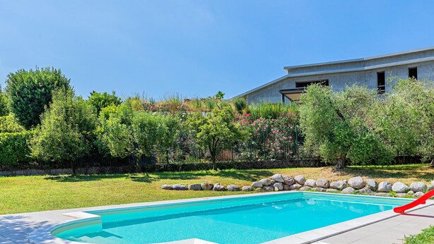 A swimming pool with a slide, surrounded by a grassy area and a stone wall.