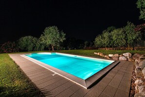 A rectangular swimming pool with a tiled deck, surrounded by a stone wall and a grassy area with trees. - Villa Elisa con Piscina by Wonderful Italy (Padenghe sul Garda)
