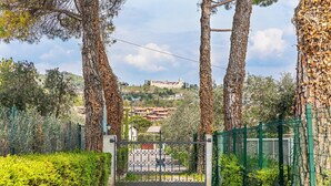 A gated pathway leading to a residential area with houses and a hill with a castle-like structure in the background.