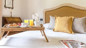 A hotel room with a bed, a bedside table with a lamp, a tray with breakfast items, and a magazine on the bed.