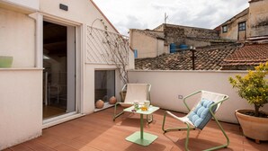 A patio with a table and chairs, a potted plant, and a view of neighboring buildings.