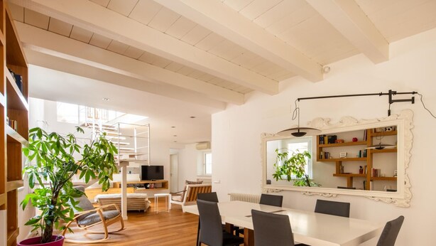 A modern living room with a dining area, a staircase, and a large mirror.