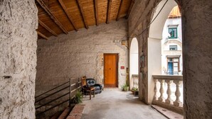 A narrow corridor with a wooden ceiling, a door at the end, and a balcony with a balustrade.