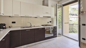 Une cuisine moderne avec des meubles de couleur sombre, une cuisinière à gaz et une grande fenêtre donnant sur un balcon.
