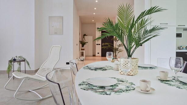 Un coin repas avec une table ronde dressée pour quatre personnes, entourée de chaises, d’une plante en pot et d’un tableau encadré accroché au mur.