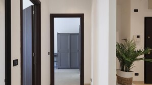 Un couloir avec une porte donnant sur une pièce, une plante en pot sur une table et un thermostat au mur.