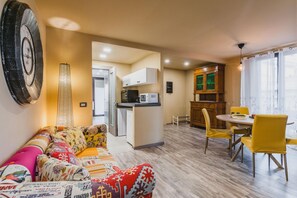 A compact living space with a sofa, a dining table with chairs, a kitchenette, and a wooden cabinet. - Ursino Apartment With Balcony by Wonderful Italy (Catania)