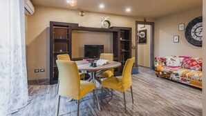 A dining area with a round table, four yellow chairs, a television, and a bookshelf. - Ursino Apartment With Balcony by Wonderful Italy (Catania)