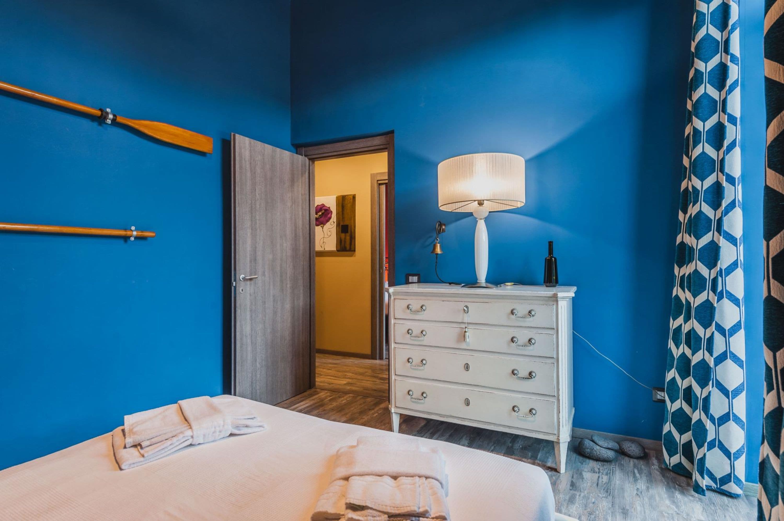 Una camera d'albergo con un letto, una cassettiera, una lampada e una porta che dà su un'altra stanza.