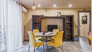 A dining area with a round table and four yellow chairs, a television, and a bookshelf. - Ursino Apartment With Balcony by Wonderful Italy (Catania)