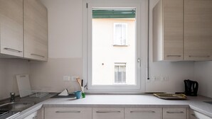 Een moderne keuken met lichte houten kastjes, een roestvrijstalen spoelbak en een raam met uitzicht op een gebouw.