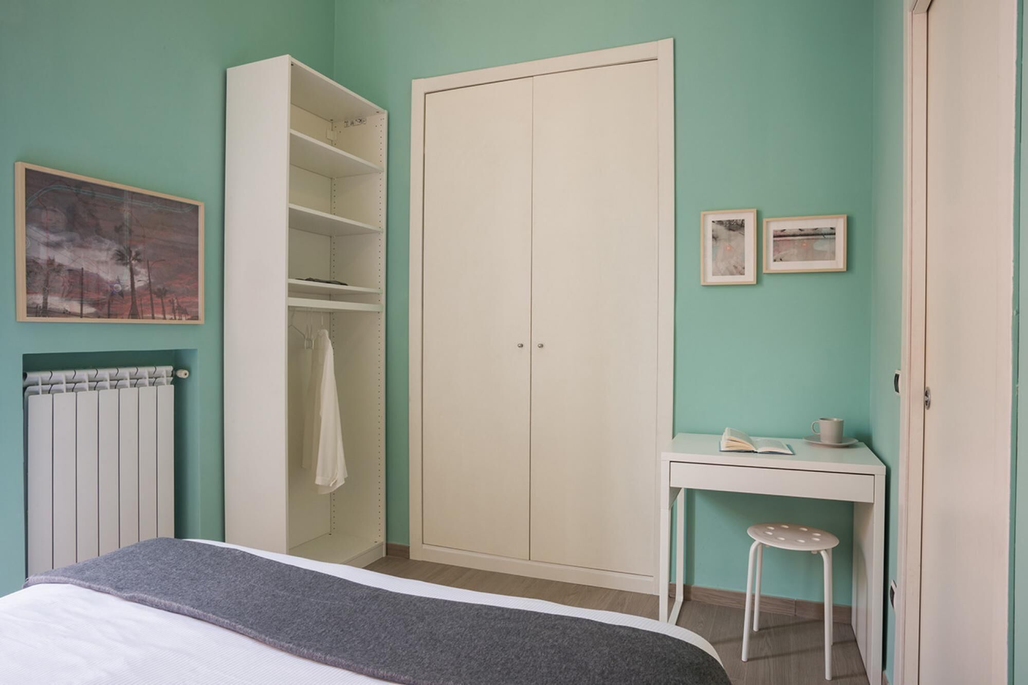 Un dormitorio con cama, armario, escritorio con silla y radiador.