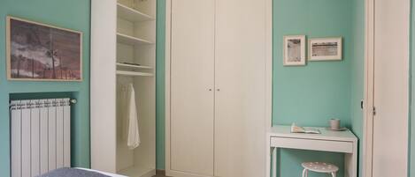 Un dormitorio con cama, armario, escritorio con silla y radiador.