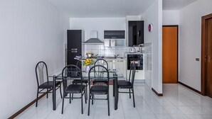 A modern kitchen with white cabinets, a black countertop, and a glass dining table with black chairs. - Artemisia B 1 con Piscina by Wonderful Italy (Sirmione)