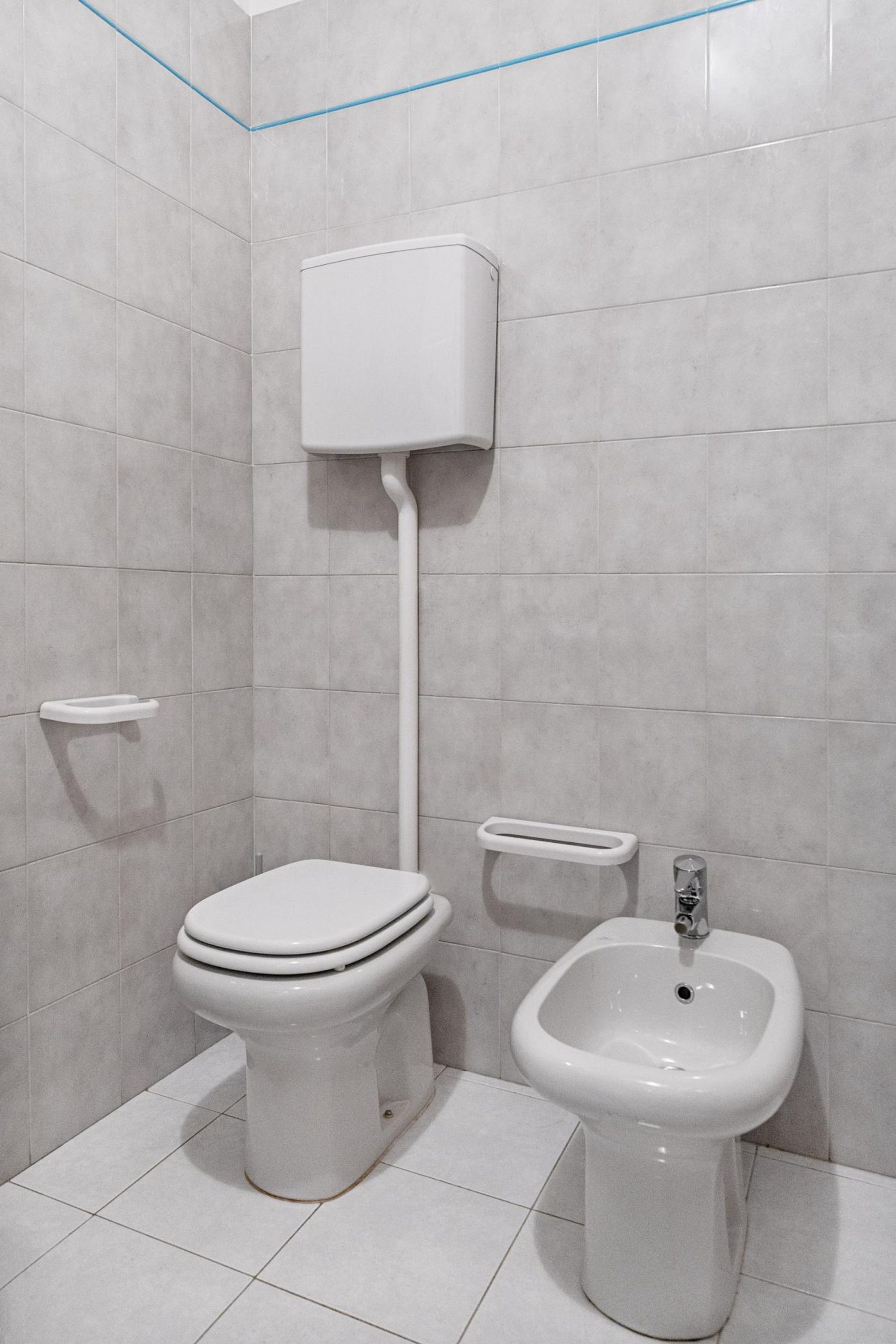 A bathroom with a toilet, bidet, and a wall-mounted tank.