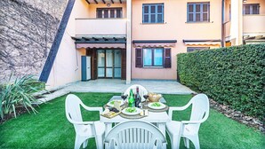 A patio with a table set for a meal, surrounded by a well-maintained lawn and a building with a sloped roof. - Artemisia B 1 con Piscina by Wonderful Italy (Sirmione)