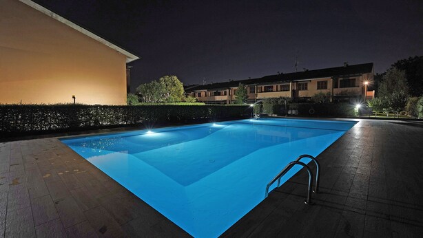 A swimming pool with a blue tint, surrounded by a paved deck and a low hedge. - Artemisia B 1 con Piscina by Wonderful Italy (Sirmione)