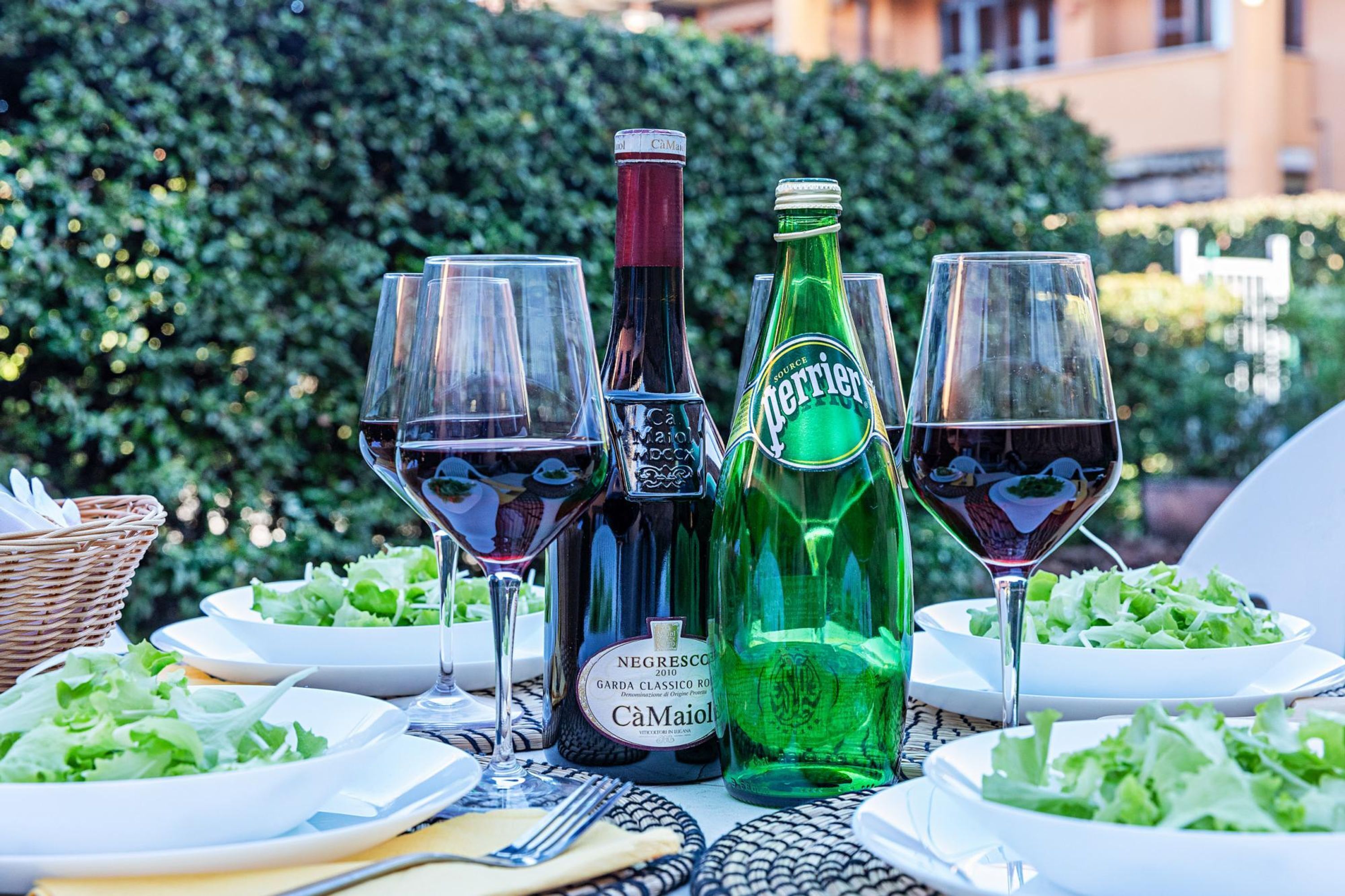 A table set with wine glasses, bottles, and plates of salad.