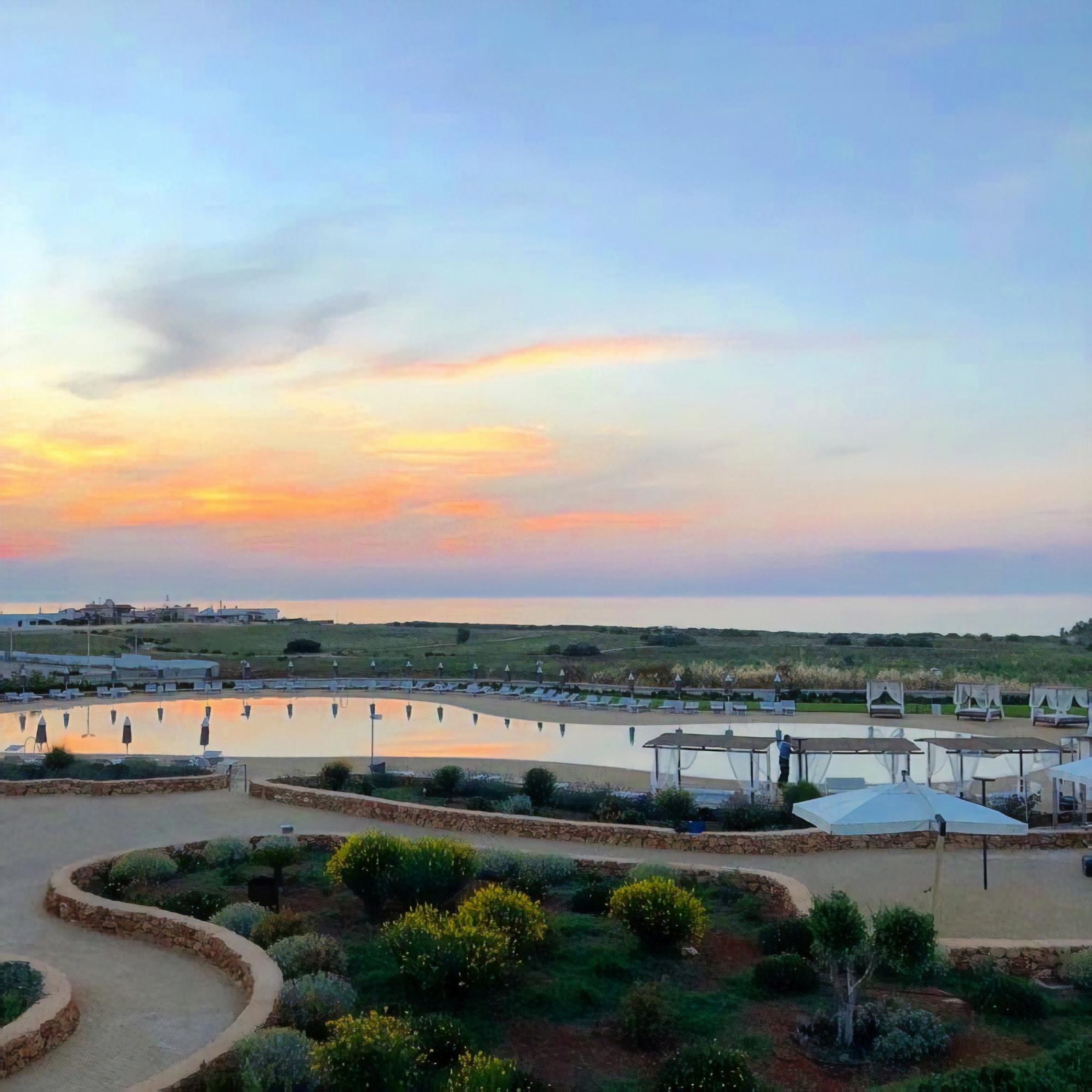 Ein Resort mit Pool, Liegestühlen und einem malerischen Sonnenuntergang.