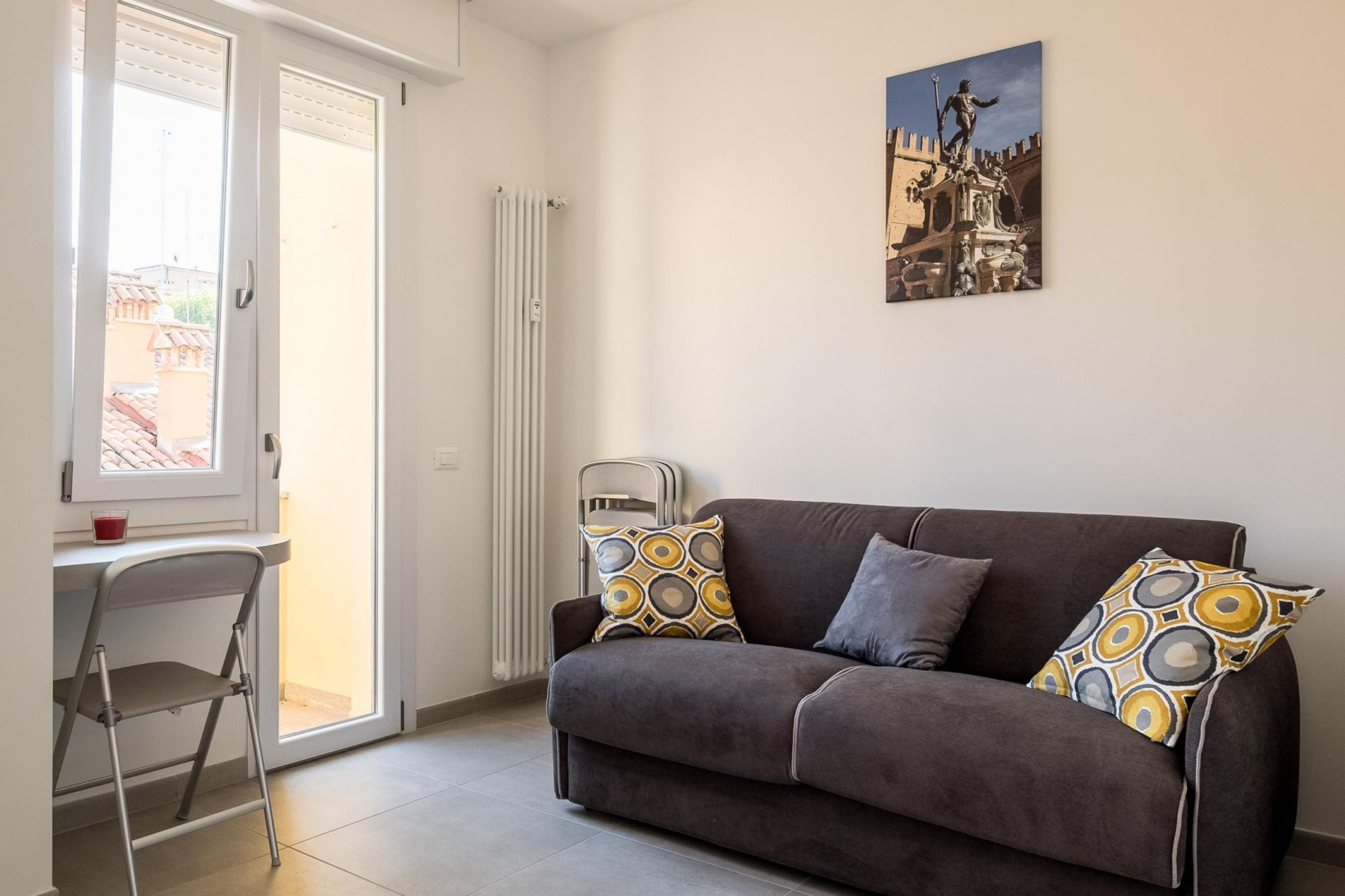A living room with a sofa, two patterned cushions, a radiator, a window, and a painting on the wall.