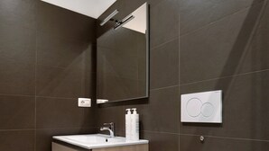 A modern bathroom with dark tiled walls, a wooden vanity, a white toilet, and a mirror. - Cineteca Grey Studio I by Wonderful Italy (Bologna)