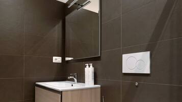 Un bagno moderno con pareti piastrellate scure, un mobile lavabo in legno, un water bianco e uno specchio.