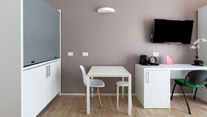 A compact room with a white desk, two chairs, a flat-screen TV, and a small cabinet. - Cineteca Grey Studio I by Wonderful Italy (Bologna)