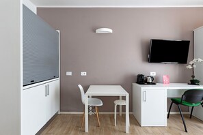 A compact room with a white desk, two chairs, a flat-screen TV, and a small cabinet.