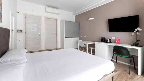 A hotel room with a large bed, a desk with a chair, a television, and a small table with a plant.