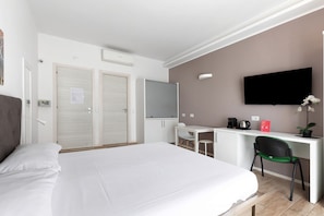 Une chambre d’hôtel avec un grand lit, un bureau avec une chaise, une télévision et une petite table avec une plante.
