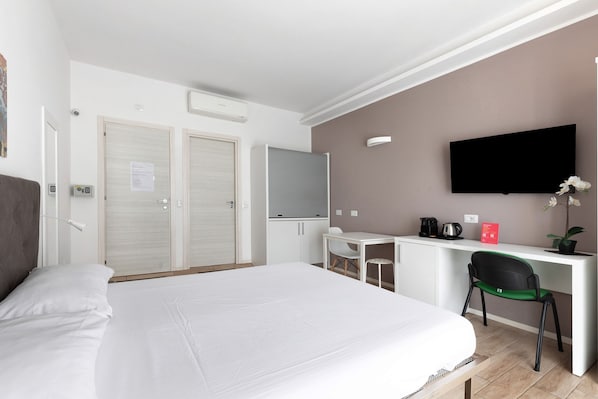A hotel room with a large bed, a desk with a chair, a television, and a small table with a plant.