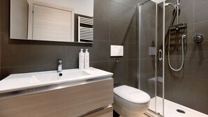 A modern bathroom with a large mirror, a white sink, a toilet, and a glass-enclosed shower area.